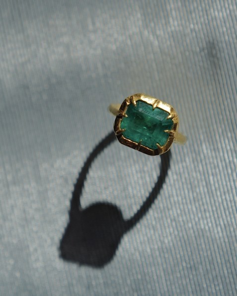 Emerald ring held in a hand-formed gold claw bezel, on silver-blue silk